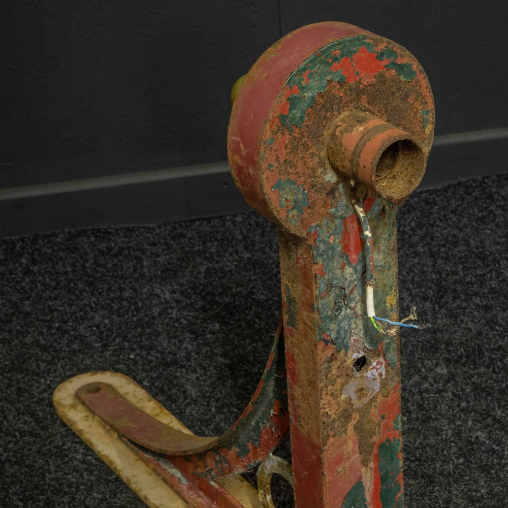 A heavy red painted cast iron wall bracket with a curved support bar and circular motif, showing distressed paint and metal details. View X