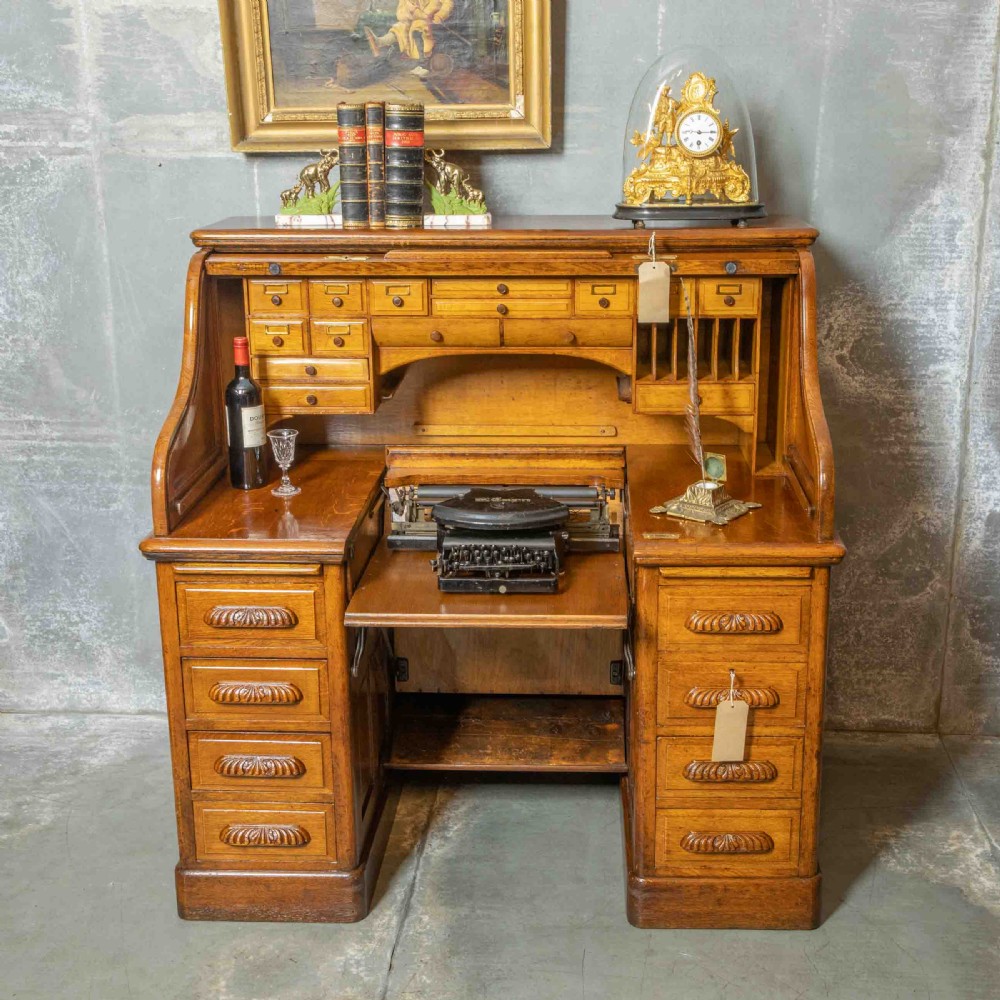 An Edwardian golden oak roll top desk featuring a flexible tambour shutter, fitted interior drawers, slotted pigeonholes, and twin pedestal bases with carved cup handles. View II