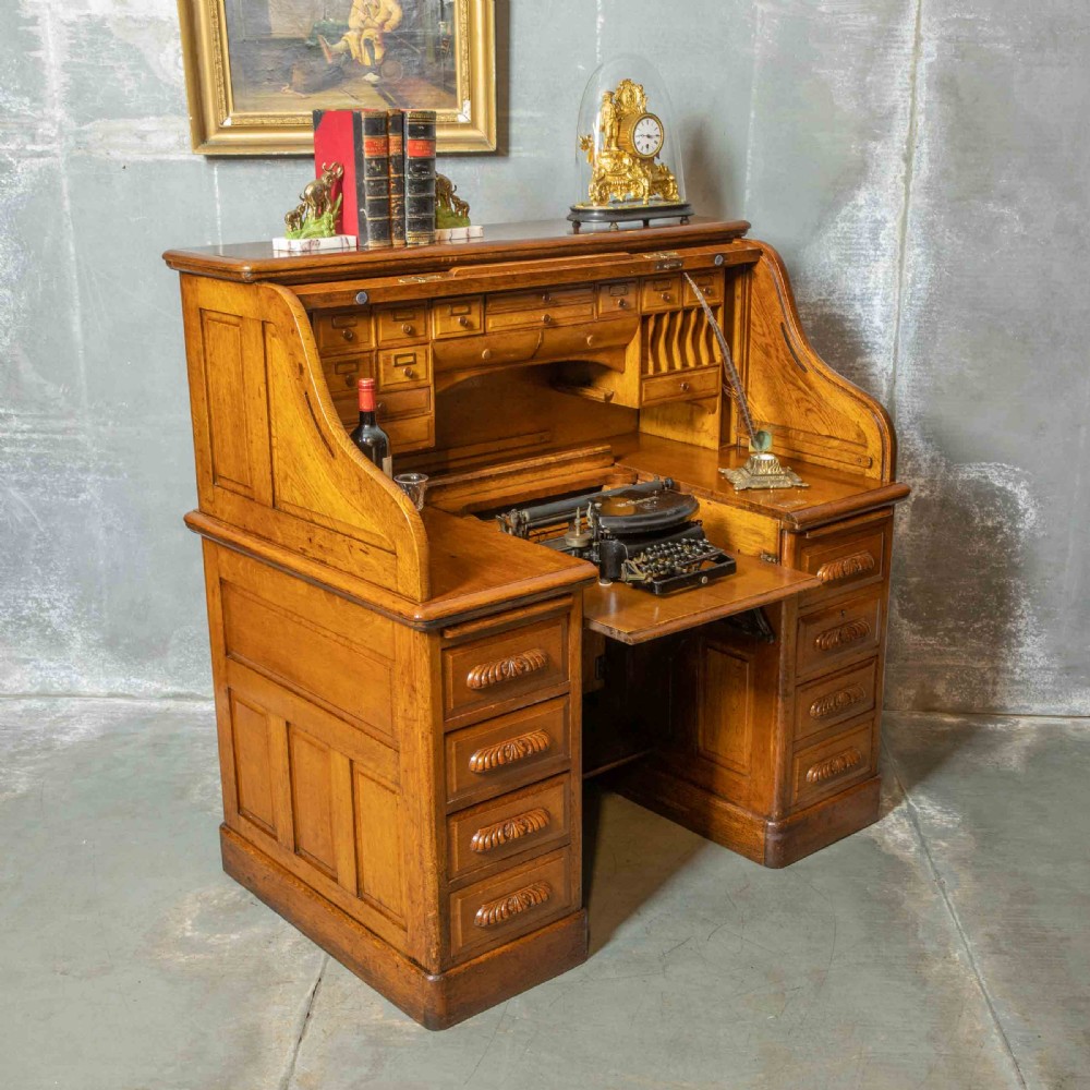An Edwardian golden oak roll top desk featuring a flexible tambour shutter, fitted interior drawers, slotted pigeonholes, and twin pedestal bases with carved cup handles. View III