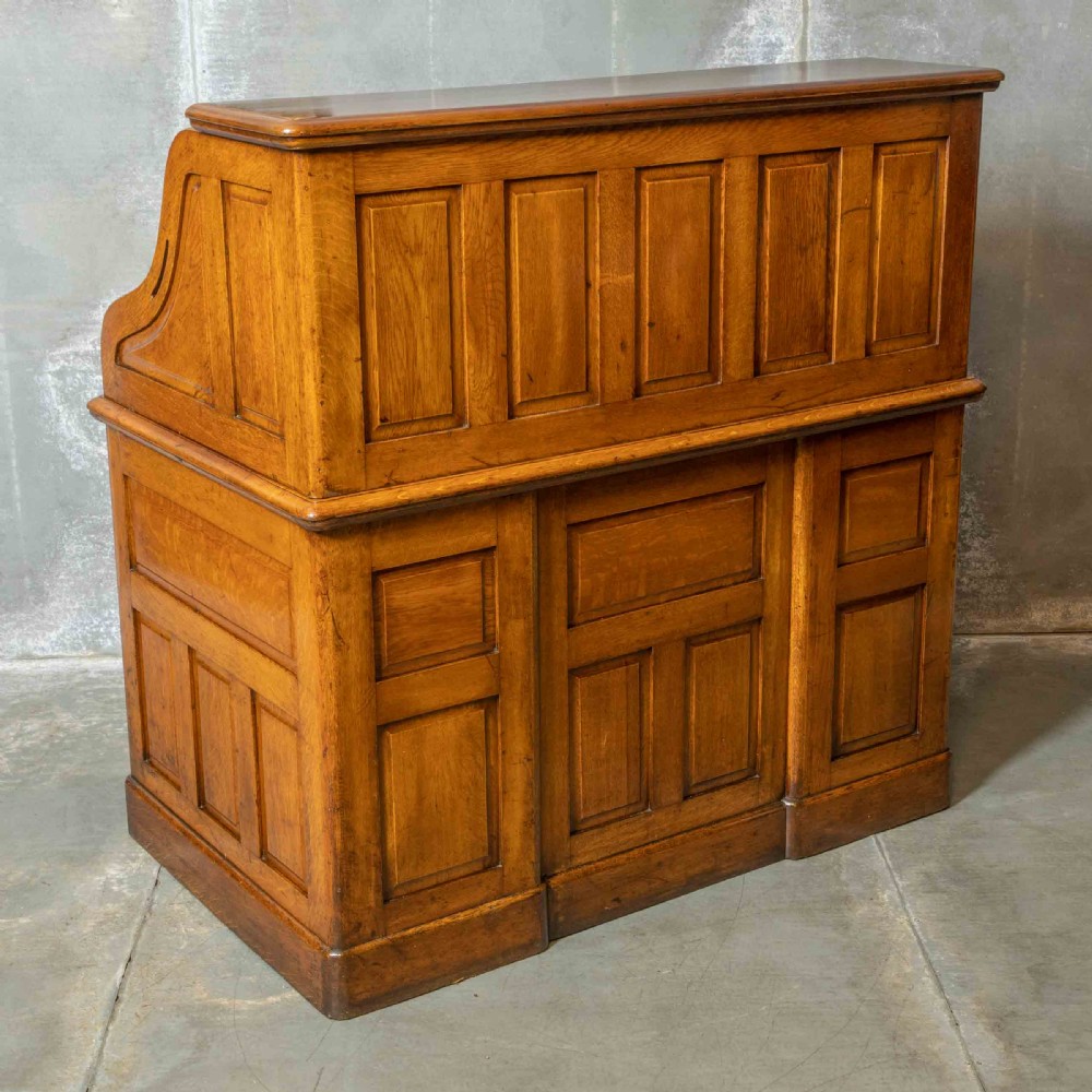 An Edwardian golden oak roll top desk featuring a flexible tambour shutter, fitted interior drawers, slotted pigeonholes, and twin pedestal bases with carved cup handles. View VI