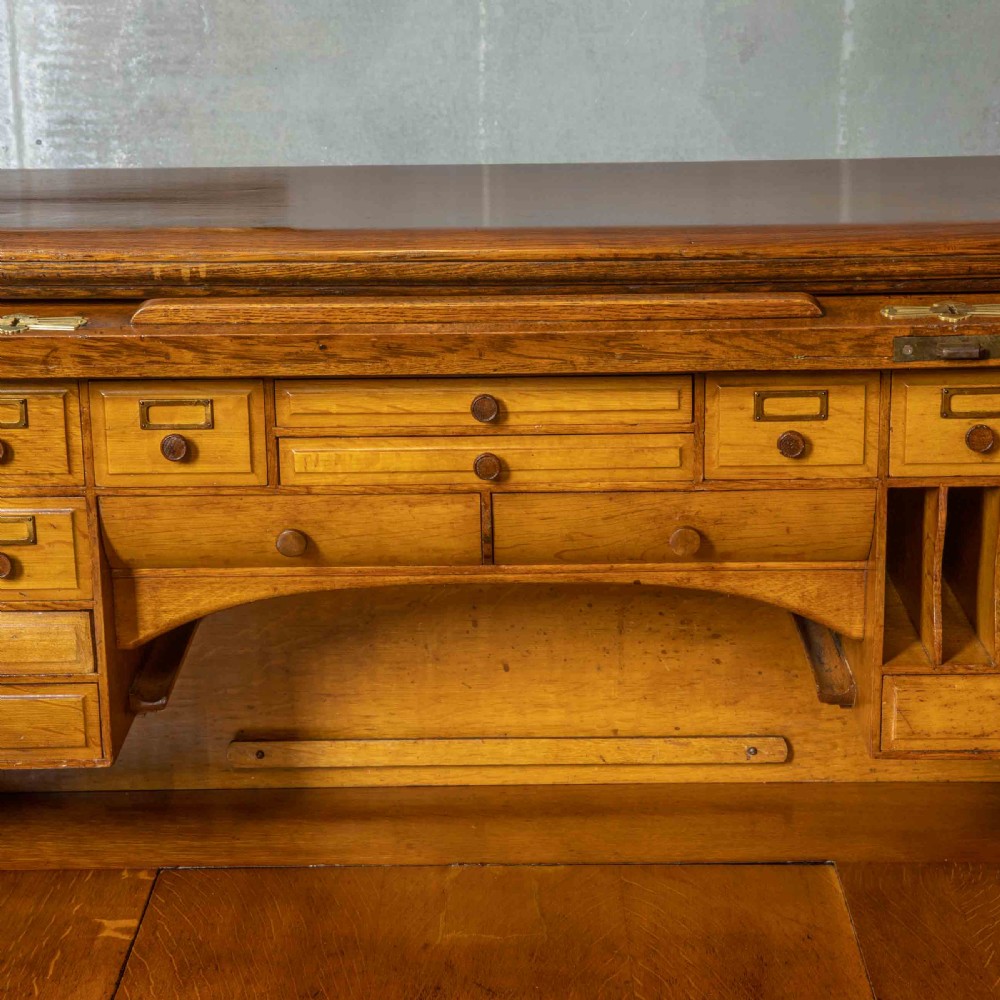 An Edwardian golden oak roll top desk featuring a flexible tambour shutter, fitted interior drawers, slotted pigeonholes, and twin pedestal bases with carved cup handles. View XIII