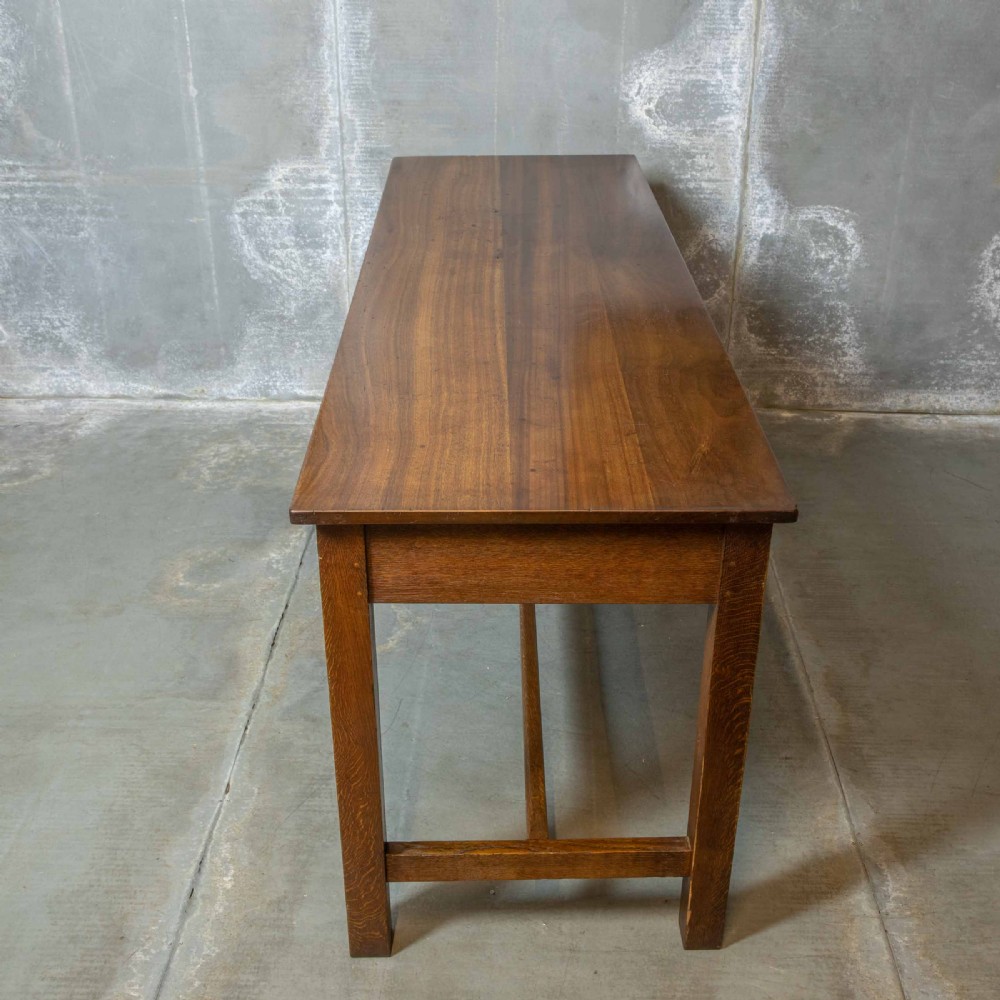 A long, tall oak refectory table featuring three frieze drawers with brass handles, straight legs, and a low H-stretcher base. View III
