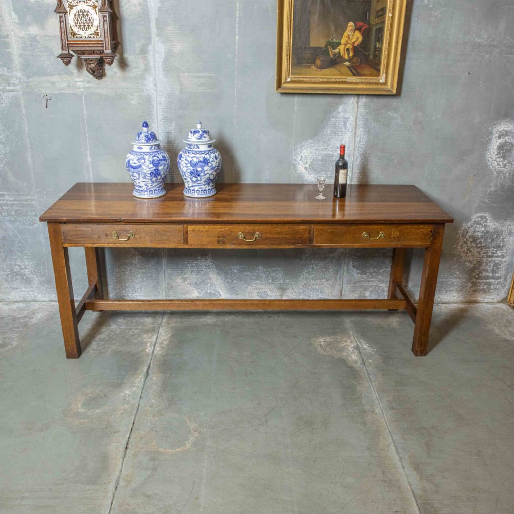 A long, tall oak refectory table featuring three frieze drawers with brass handles, straight legs, and a low H-stretcher base. View IV