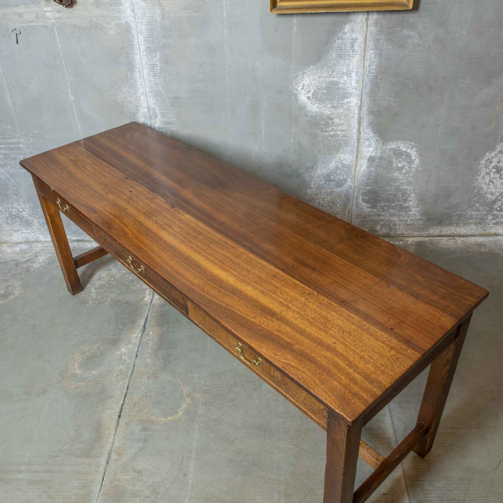 A long, tall oak refectory table featuring three frieze drawers with brass handles, straight legs, and a low H-stretcher base. View V
