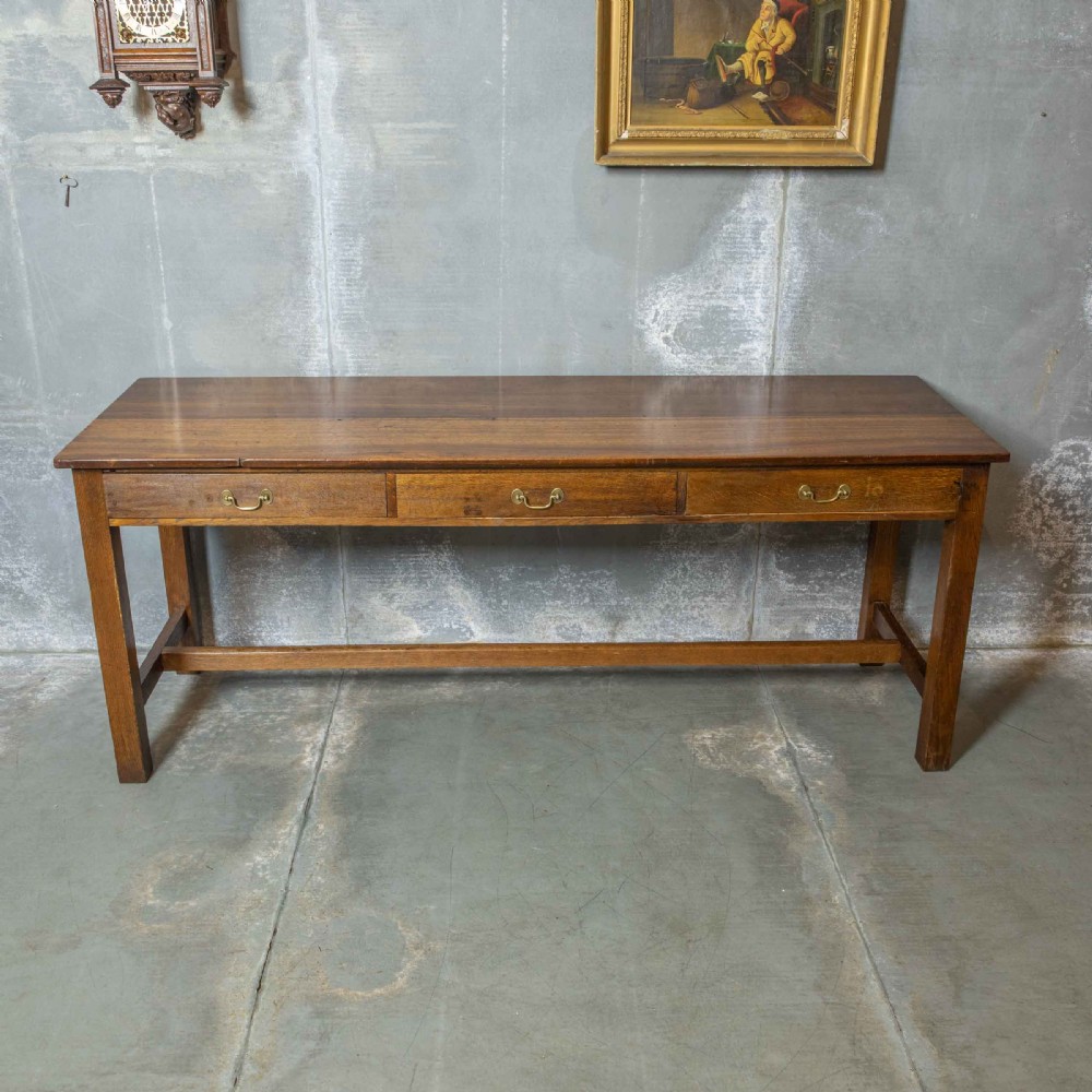 A long, tall oak refectory table featuring three frieze drawers with brass handles, straight legs, and a low H-stretcher base. View VI