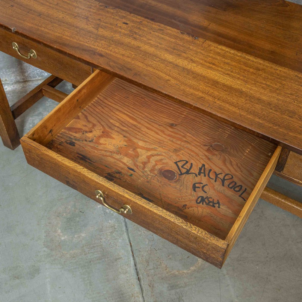 A long, tall oak refectory table featuring three frieze drawers with brass handles, straight legs, and a low H-stretcher base. View VII