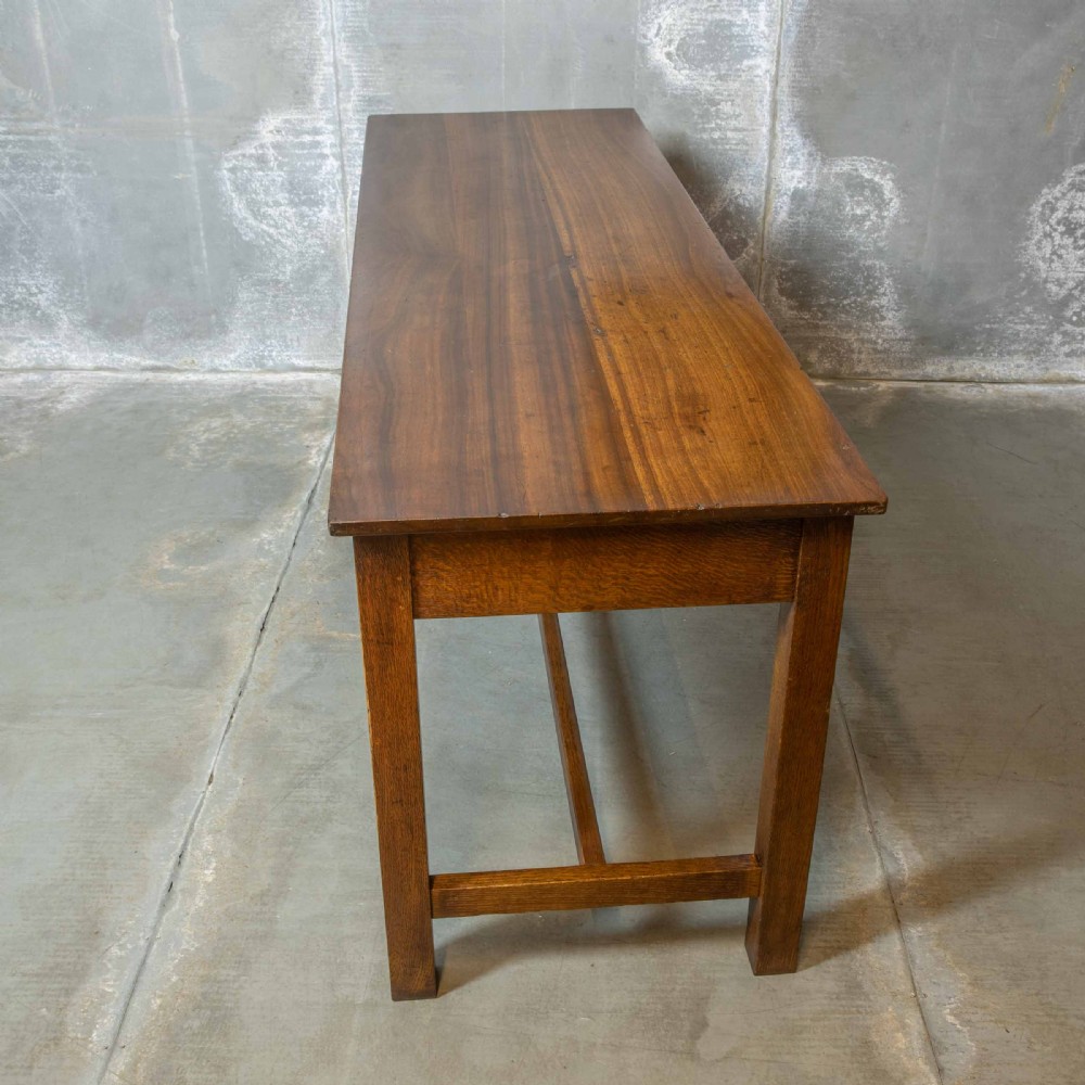 A long, tall oak refectory table featuring three frieze drawers with brass handles, straight legs, and a low H-stretcher base. View IX