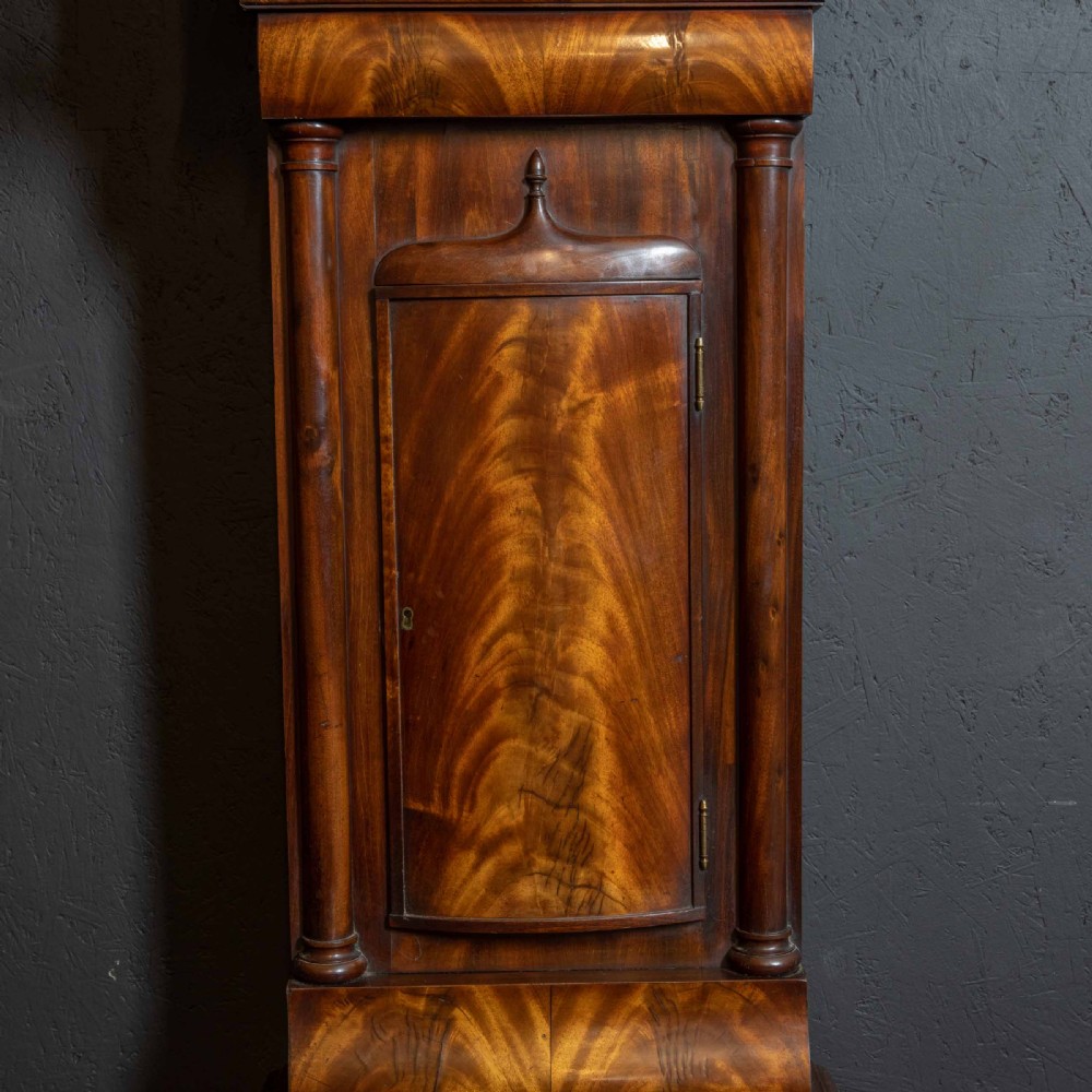 An antique Scottish mahogany longcase clock featuring a swan neck pediment, turned hood columns, flame mahogany trunk door, and a hand-painted dial. View XI
