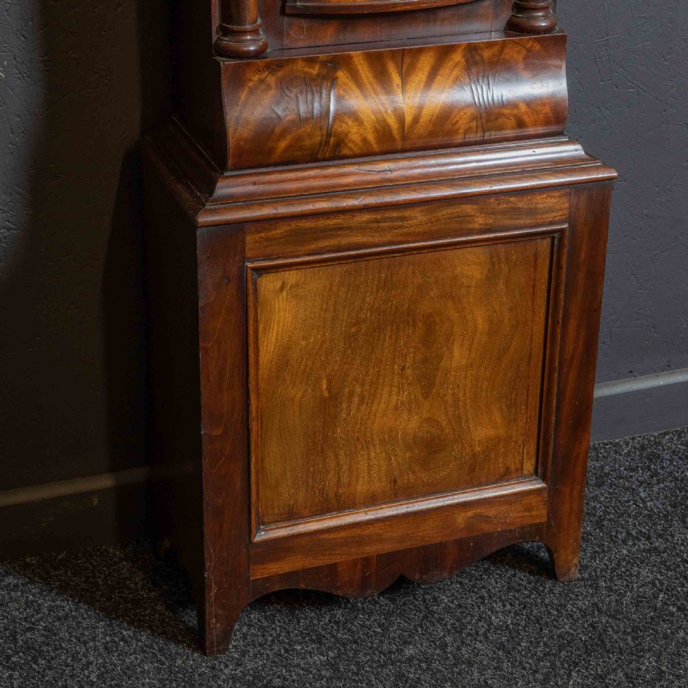 An antique Scottish mahogany longcase clock featuring a swan neck pediment, turned hood columns, flame mahogany trunk door, and a hand-painted dial. View XII