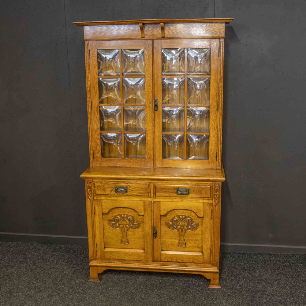 An Art Nouveau golden oak glazed bookcase featuring upper glass door panels and lower carved doors with stylised floral motifs. View III