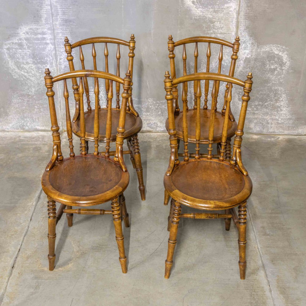 A set of four warm brown wooden bentwood dining chairs featuring spindle backrests and circular seats.