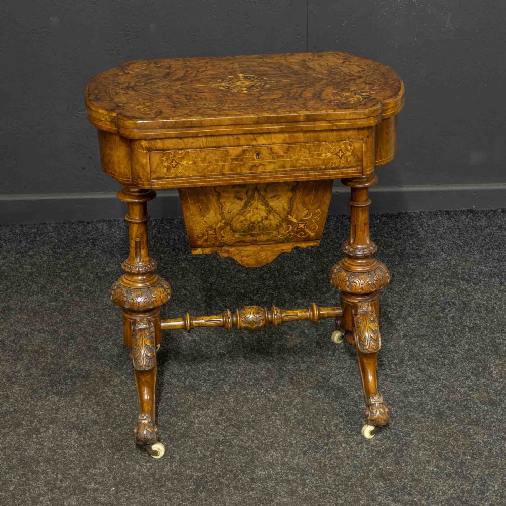 A Victorian burr walnut fold-over games and sewing table displaying an inlaid chess and backgammon board supported by carved pedestals, a stretcher base, and castors. View II