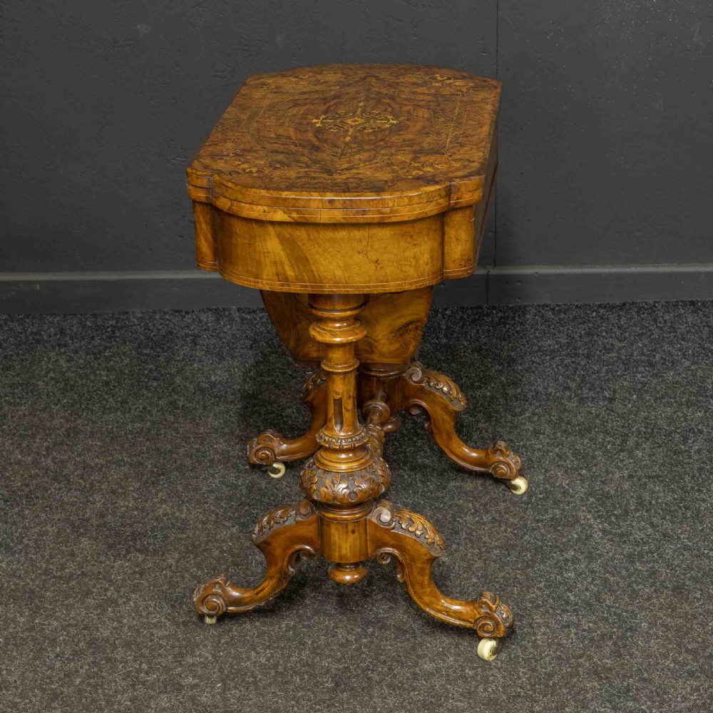 A Victorian burr walnut fold-over games and sewing table displaying an inlaid chess and backgammon board supported by carved pedestals, a stretcher base, and castors. View III