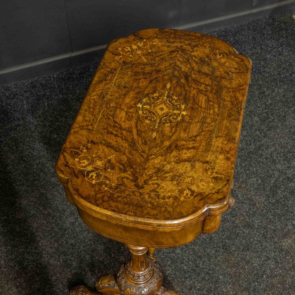 A Victorian burr walnut fold-over games and sewing table displaying an inlaid chess and backgammon board supported by carved pedestals, a stretcher base, and castors. View IV