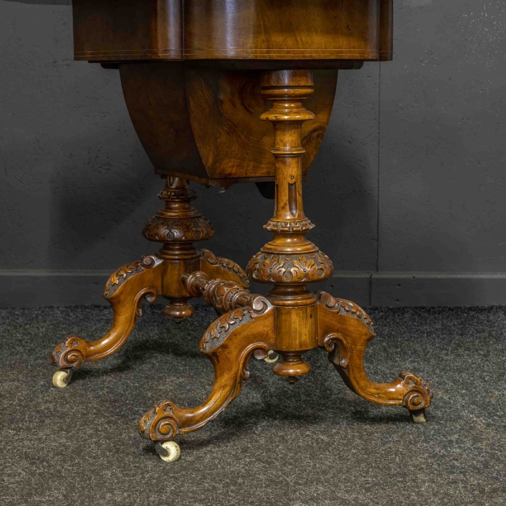 A Victorian burr walnut fold-over games and sewing table displaying an inlaid chess and backgammon board supported by carved pedestals, a stretcher base, and castors. View VII