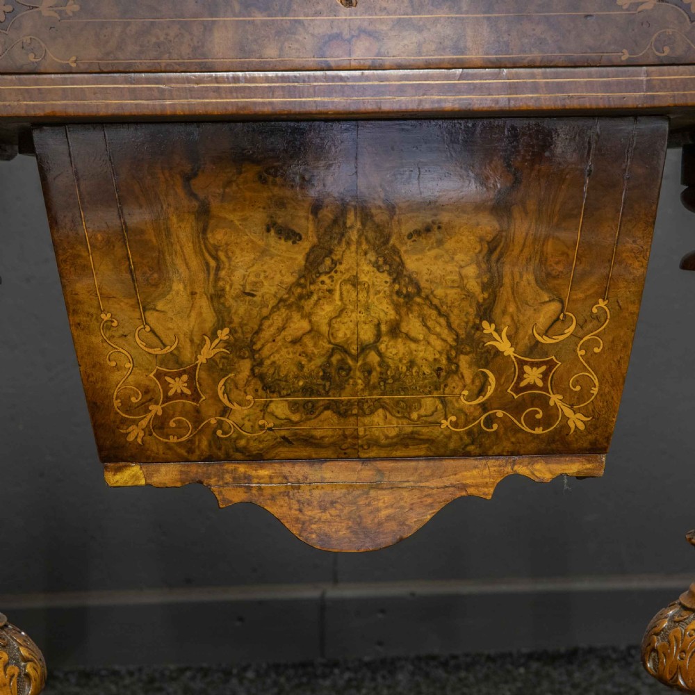 A Victorian burr walnut fold-over games and sewing table displaying an inlaid chess and backgammon board supported by carved pedestals, a stretcher base, and castors. View IX