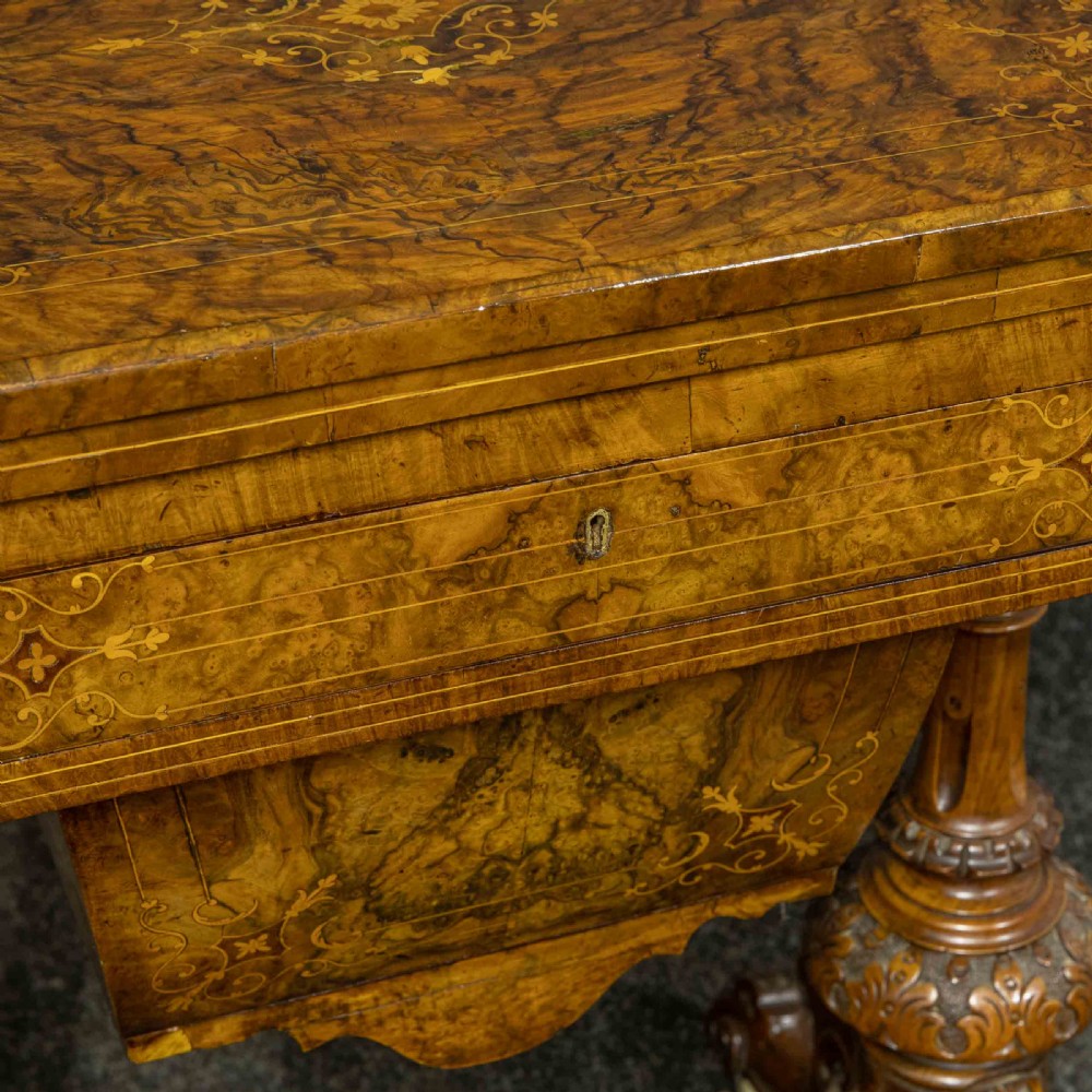 A Victorian burr walnut fold-over games and sewing table displaying an inlaid chess and backgammon board supported by carved pedestals, a stretcher base, and castors. View X