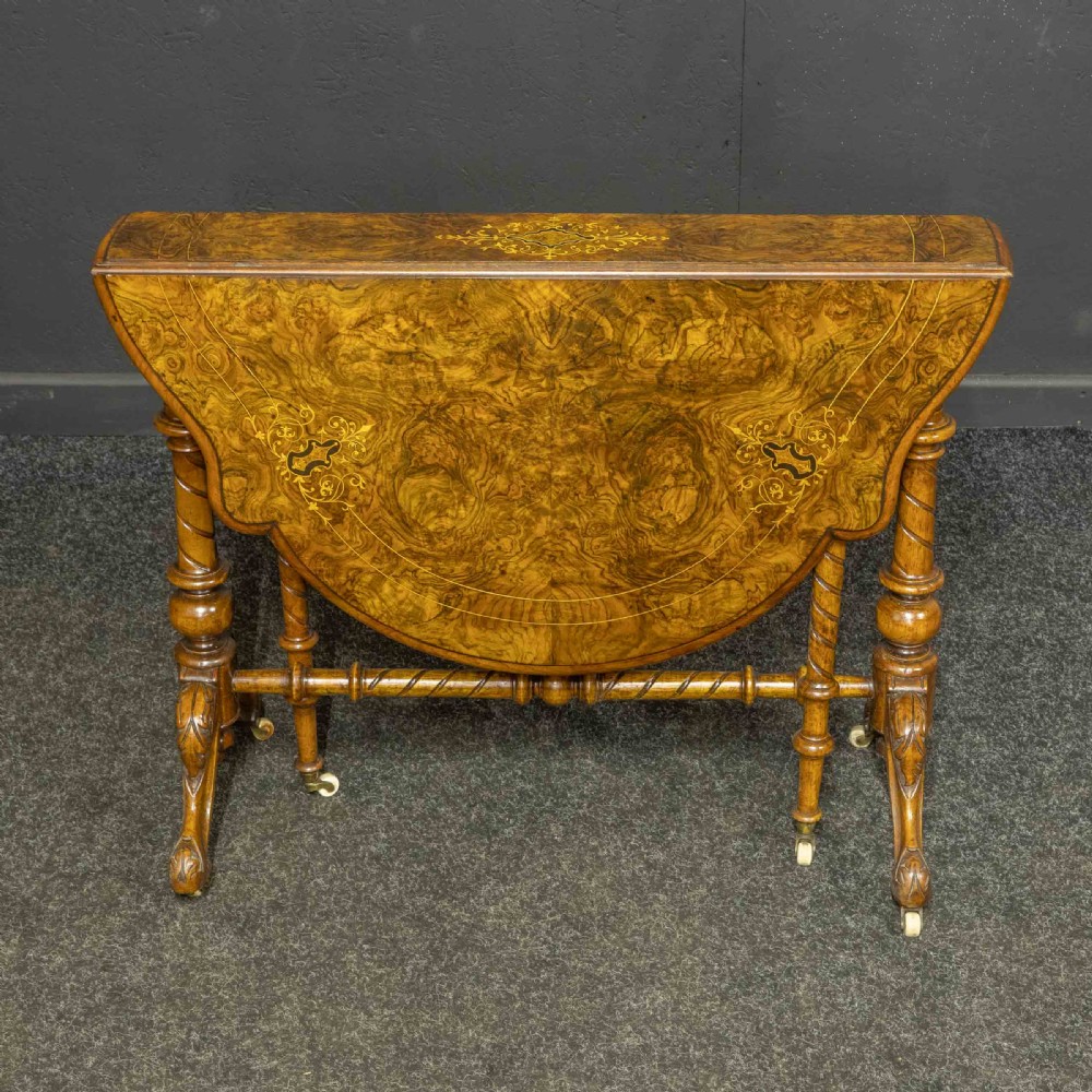 A Victorian burr walnut Sutherland drop-leaf table featuring detailed marquetry inlay, turned legs, and ceramic castors.