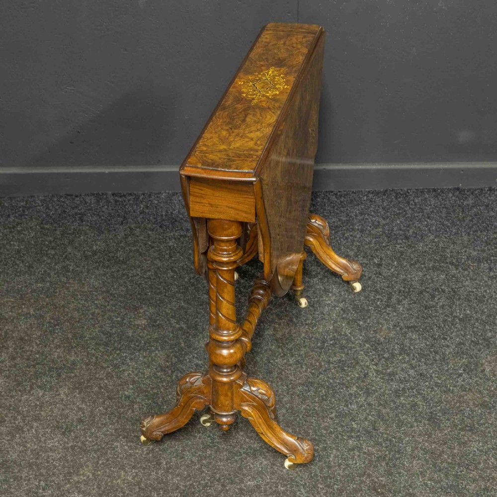 A Victorian burr walnut Sutherland drop-leaf table featuring detailed marquetry inlay, turned legs, and ceramic castors. View VI