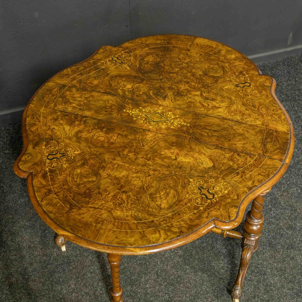 A Victorian burr walnut Sutherland drop-leaf table featuring detailed marquetry inlay, turned legs, and ceramic castors. View X