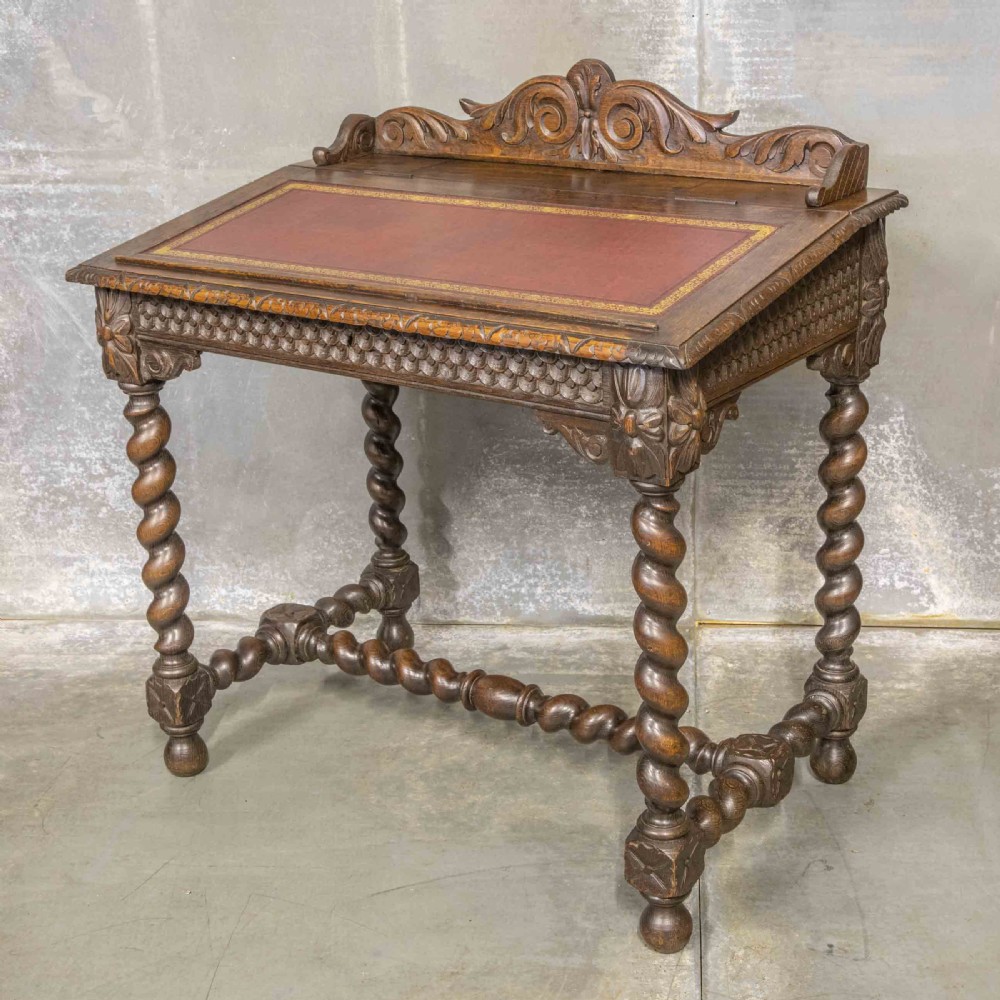 A Victorian carved oak writing desk featuring a sloped red leather surface, barley twist legs, and carved gallery details.