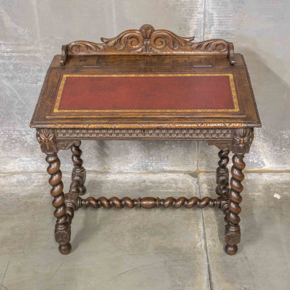 A Victorian carved oak writing desk featuring a sloped red leather surface, barley twist legs, and carved gallery details. View II