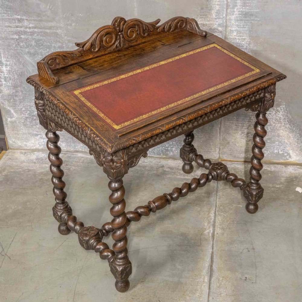 A Victorian carved oak writing desk featuring a sloped red leather surface, barley twist legs, and carved gallery details. View III