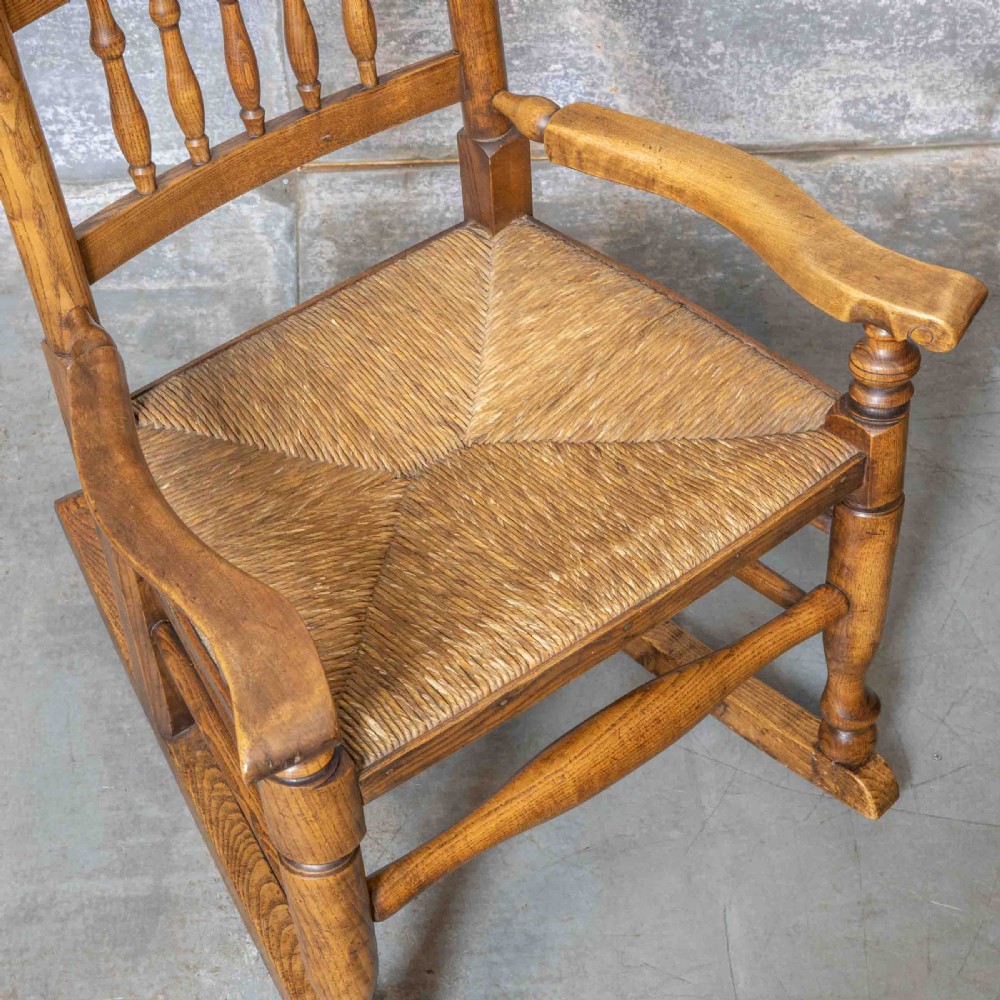 A pair of matching Victorian country armchairs in warm wood with woven rush seats and turned spindle backs, including one rocking chair and one static armchair. View XIV