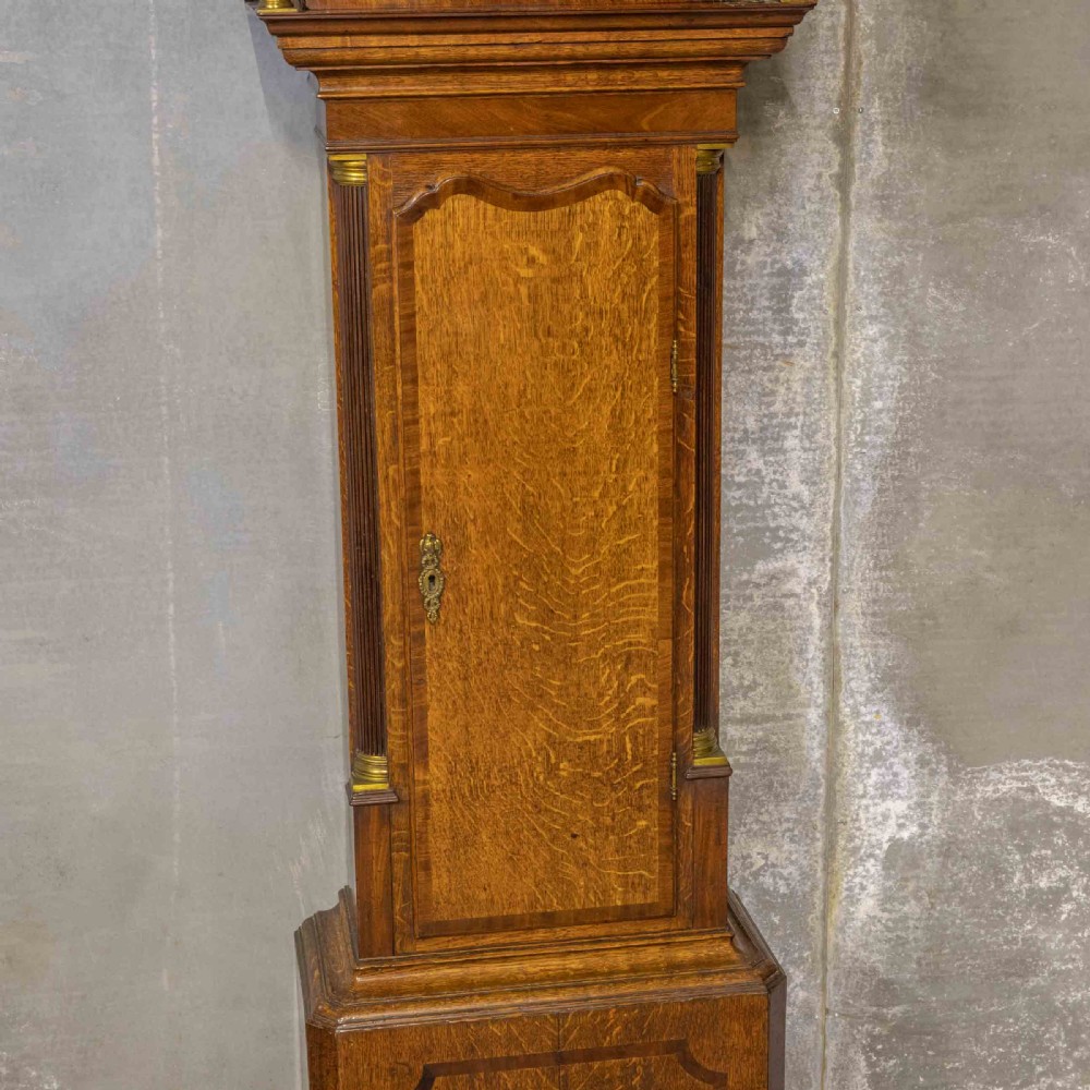 An antique Georgian oak longcase clock featuring a carved fretted pediment, brass finials, and a hand-painted square dial face. View II
