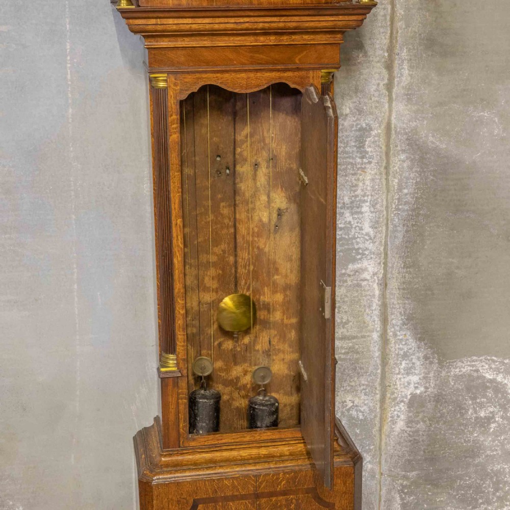An antique Georgian oak longcase clock featuring a carved fretted pediment, brass finials, and a hand-painted square dial face. View III