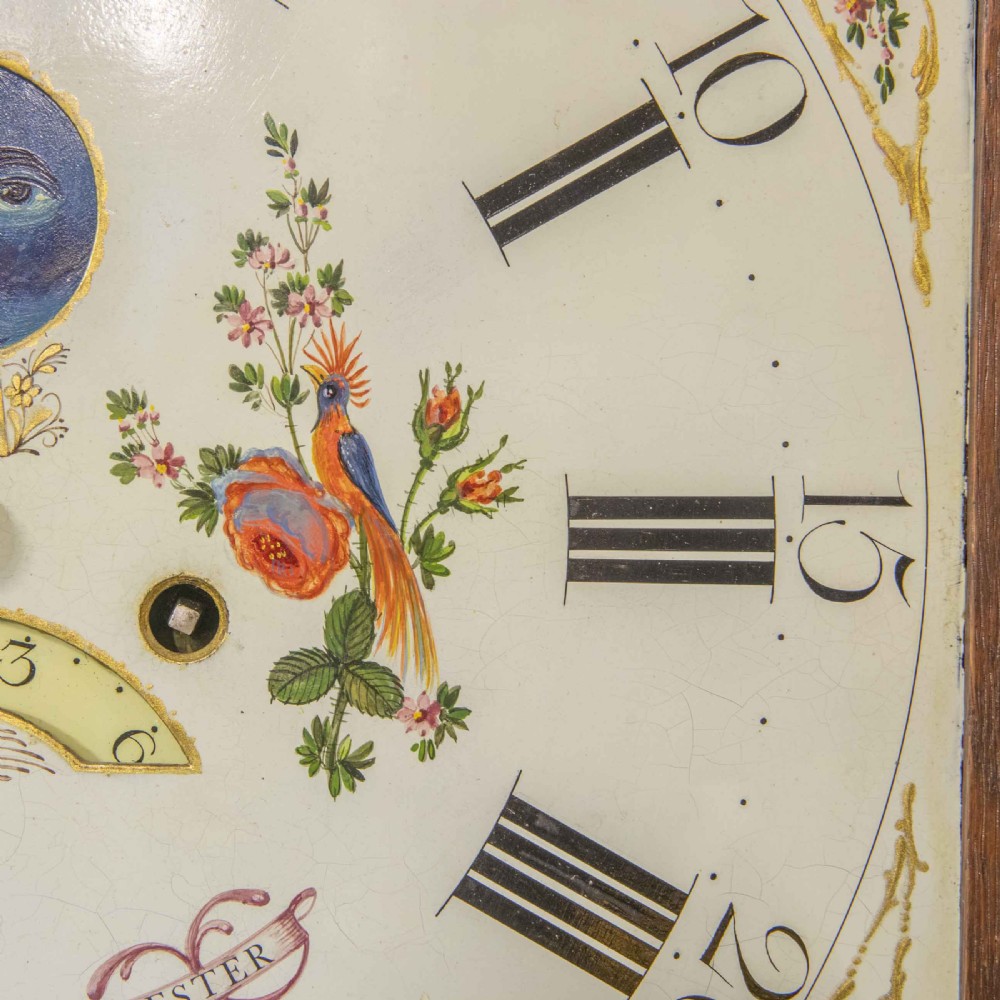 An antique Georgian oak longcase clock featuring a carved fretted pediment, brass finials, and a hand-painted square dial face. View IX