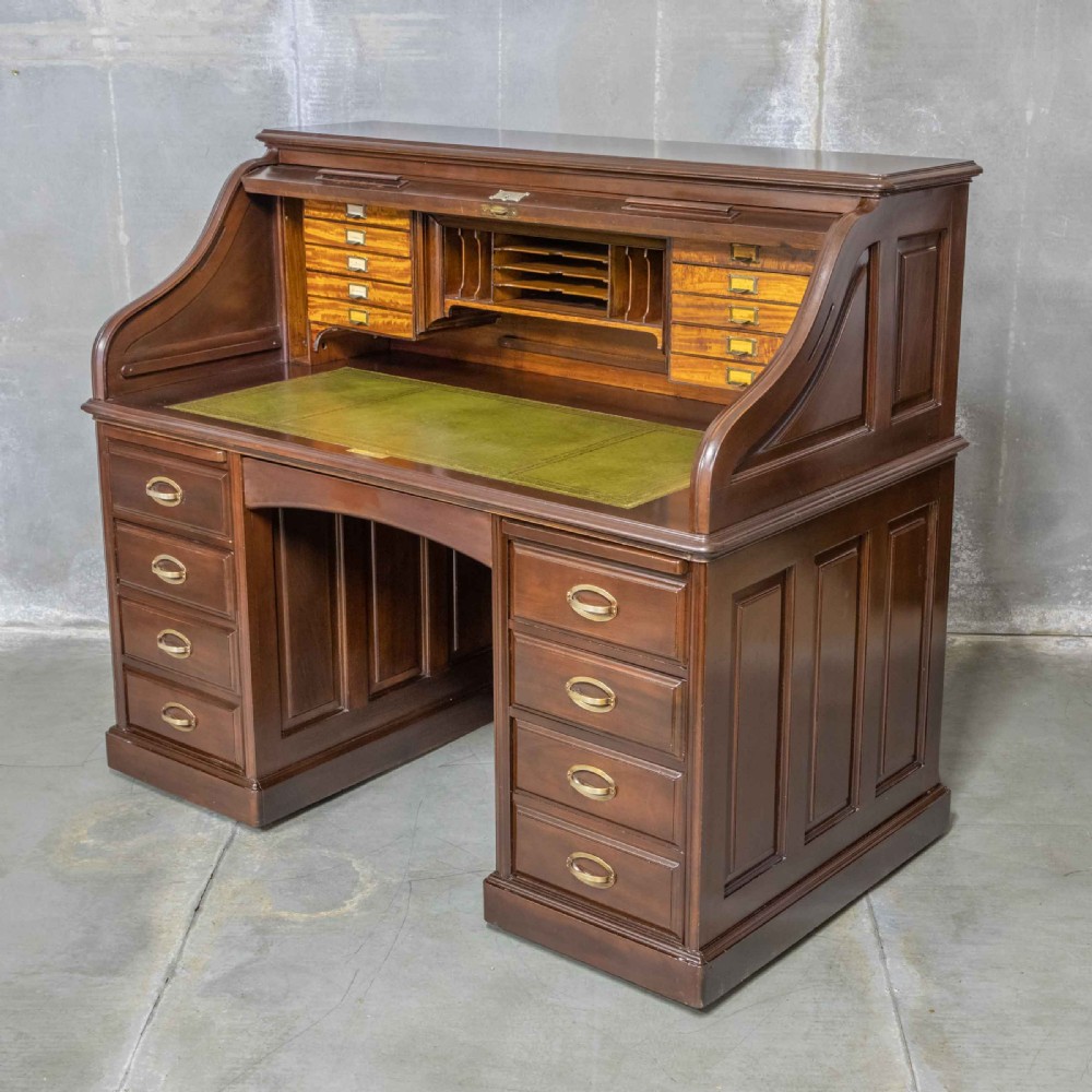 An Edwardian walnut double-pedestal roll top desk featuring a slatted tambour cover, inset green leather writing surface, multiple small interior drawers, and twin pedestal drawers with brass handles.