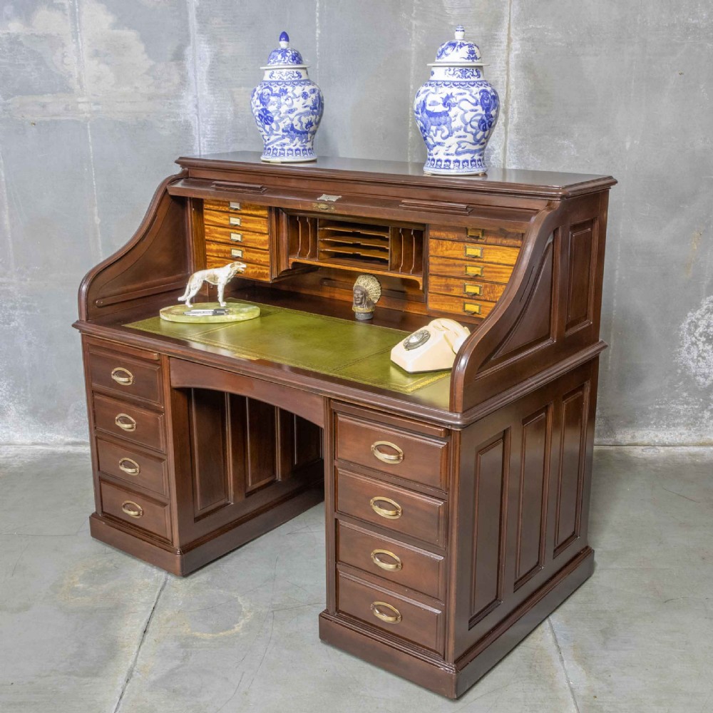 An Edwardian walnut double-pedestal roll top desk featuring a slatted tambour cover, inset green leather writing surface, multiple small interior drawers, and twin pedestal drawers with brass handles. View II