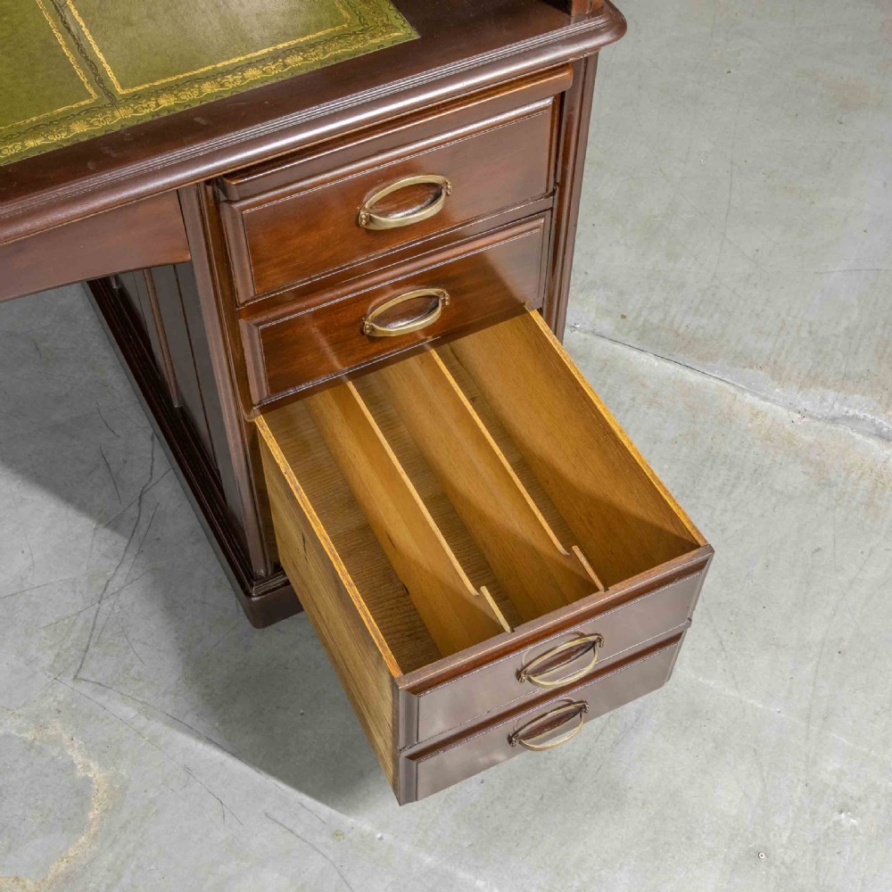 An Edwardian walnut double-pedestal roll top desk featuring a slatted tambour cover, inset green leather writing surface, multiple small interior drawers, and twin pedestal drawers with brass handles. View IV