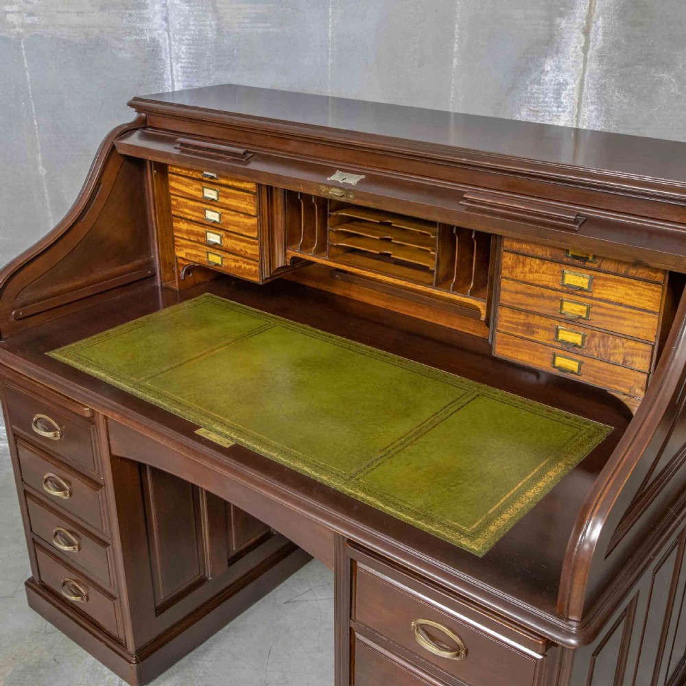 An Edwardian walnut double-pedestal roll top desk featuring a slatted tambour cover, inset green leather writing surface, multiple small interior drawers, and twin pedestal drawers with brass handles. View VI