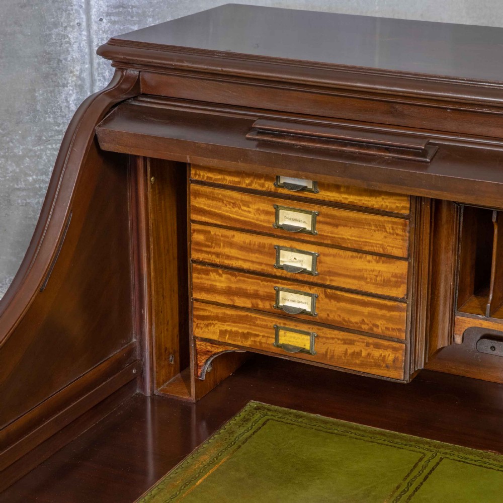 An Edwardian walnut double-pedestal roll top desk featuring a slatted tambour cover, inset green leather writing surface, multiple small interior drawers, and twin pedestal drawers with brass handles. View VII