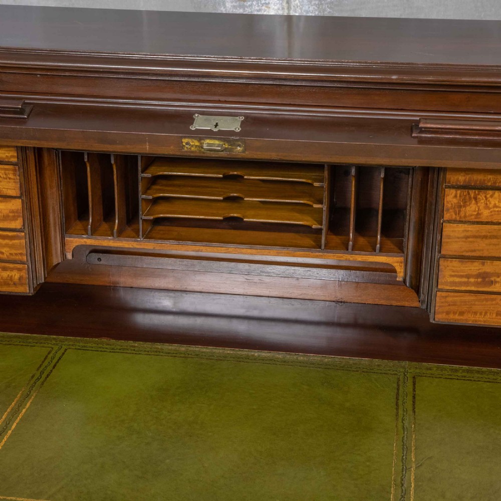 An Edwardian walnut double-pedestal roll top desk featuring a slatted tambour cover, inset green leather writing surface, multiple small interior drawers, and twin pedestal drawers with brass handles. View VIII