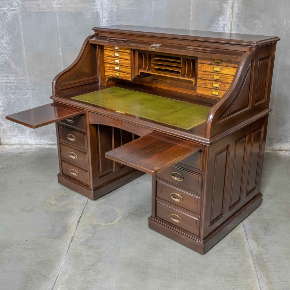 An Edwardian walnut double-pedestal roll top desk featuring a slatted tambour cover, inset green leather writing surface, multiple small interior drawers, and twin pedestal drawers with brass handles. View IX