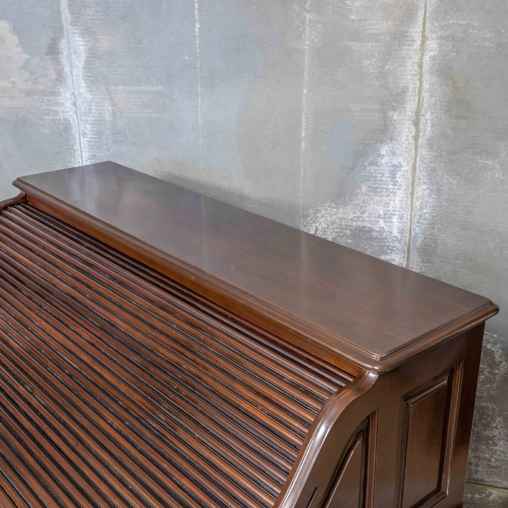 An Edwardian walnut double-pedestal roll top desk featuring a slatted tambour cover, inset green leather writing surface, multiple small interior drawers, and twin pedestal drawers with brass handles. View XII