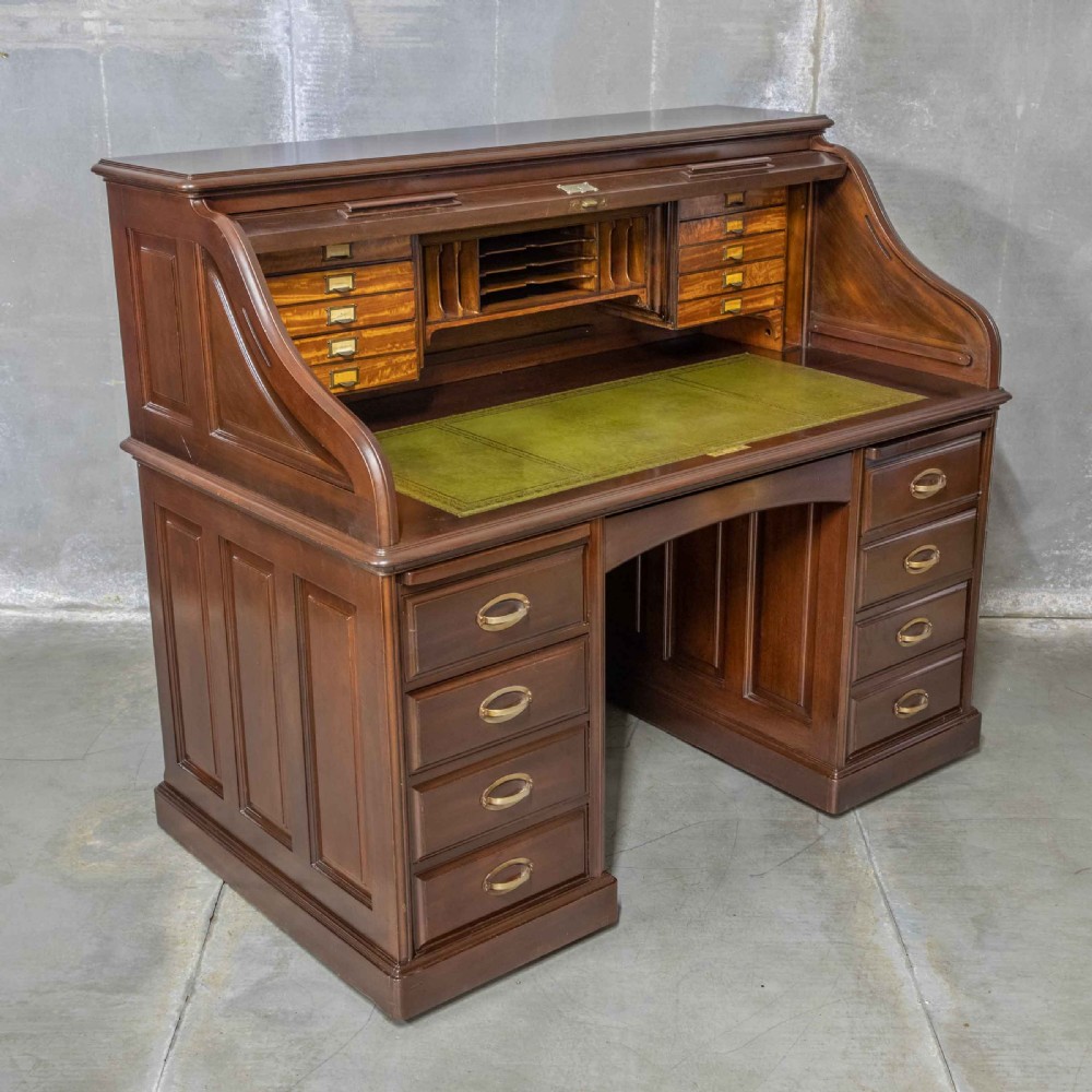 An Edwardian walnut double-pedestal roll top desk featuring a slatted tambour cover, inset green leather writing surface, multiple small interior drawers, and twin pedestal drawers with brass handles. View XV