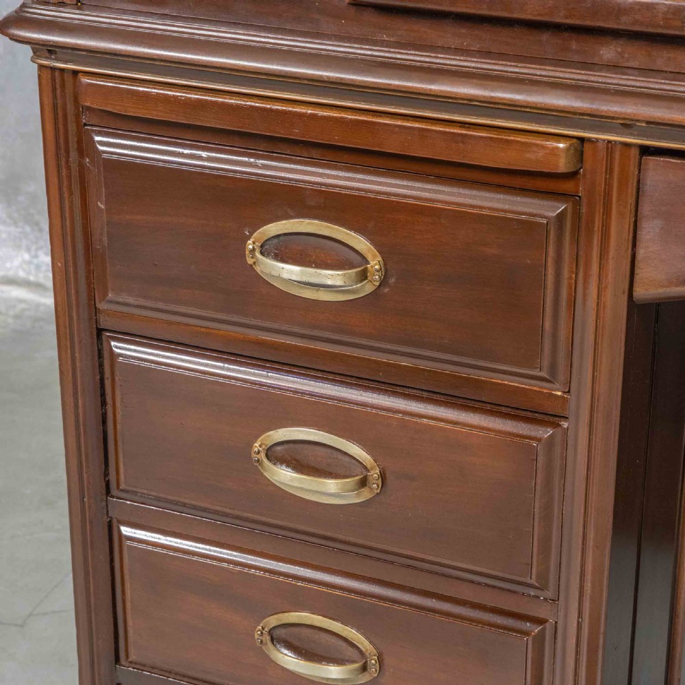 An Edwardian walnut double-pedestal roll top desk featuring a slatted tambour cover, inset green leather writing surface, multiple small interior drawers, and twin pedestal drawers with brass handles. View XXI