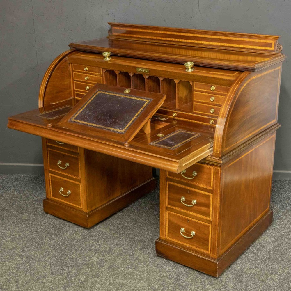 An antique mahogany cylinder desk featuring inlaid satinwood borders, a pull-out leather writing slope, fitted pigeonholes, and twin drawer pedestals.