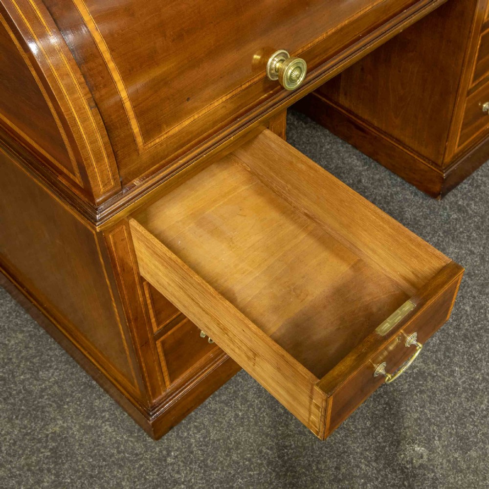 An antique mahogany cylinder desk featuring inlaid satinwood borders, a pull-out leather writing slope, fitted pigeonholes, and twin drawer pedestals. View V
