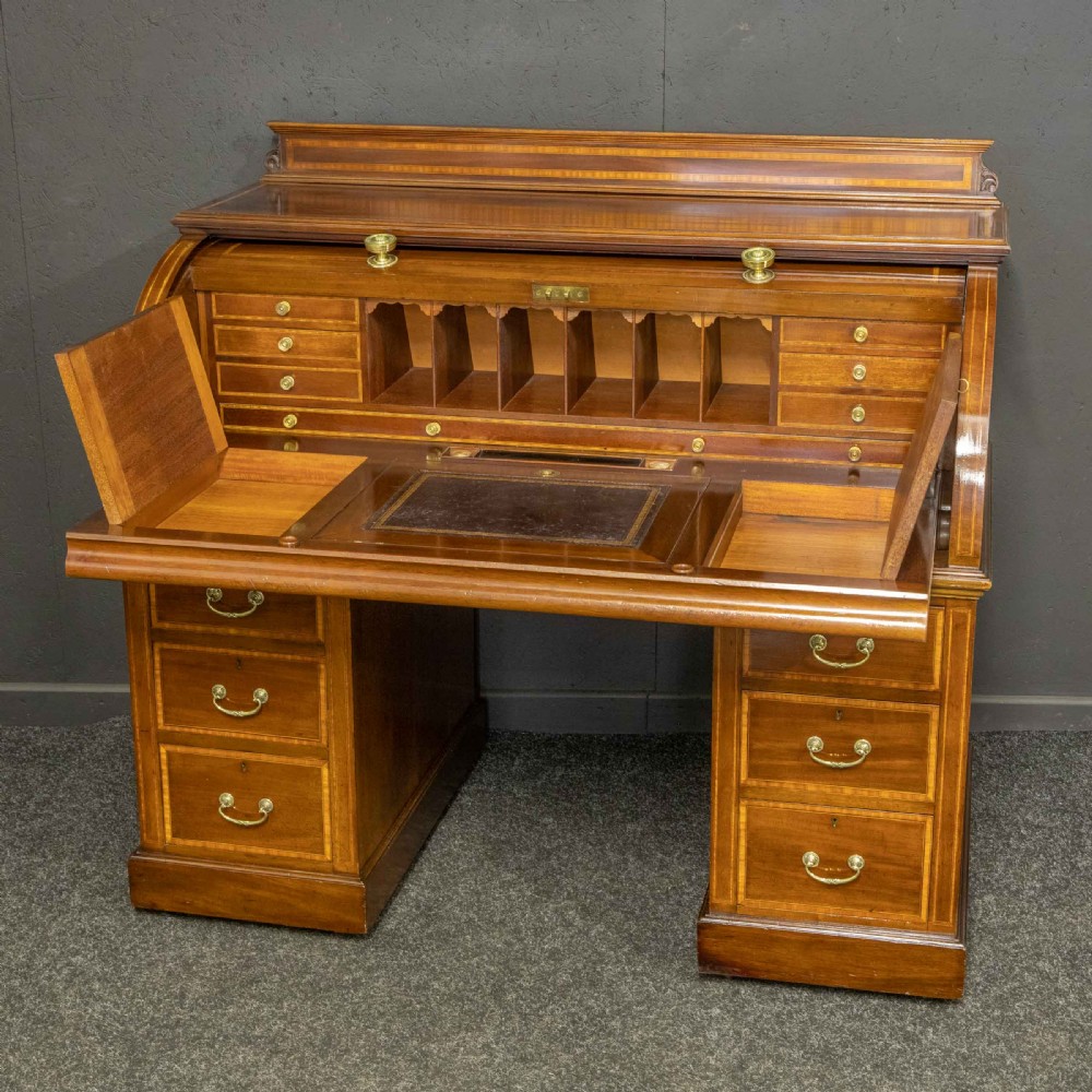 An antique mahogany cylinder desk featuring inlaid satinwood borders, a pull-out leather writing slope, fitted pigeonholes, and twin drawer pedestals. View X