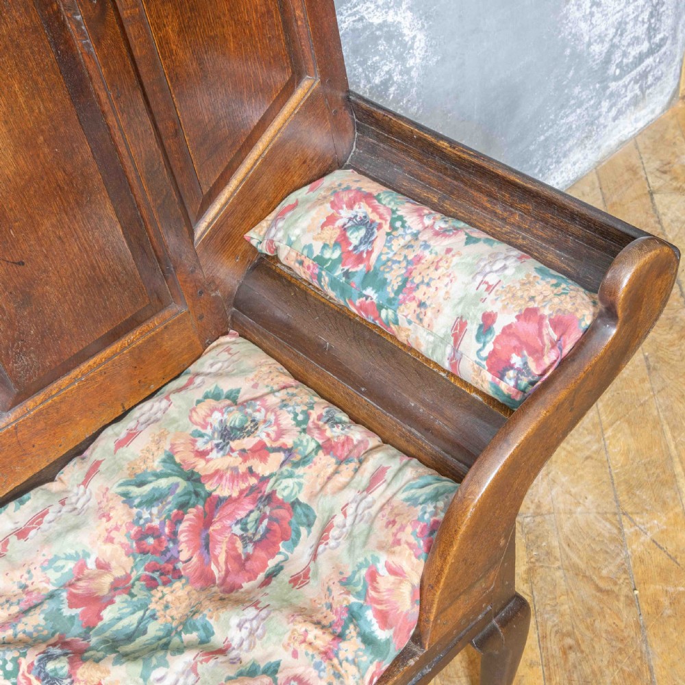 An antique dark oak sleeper settle featuring a high panelled backrest, cabriole front legs, and a floral upholstered cushion. View II