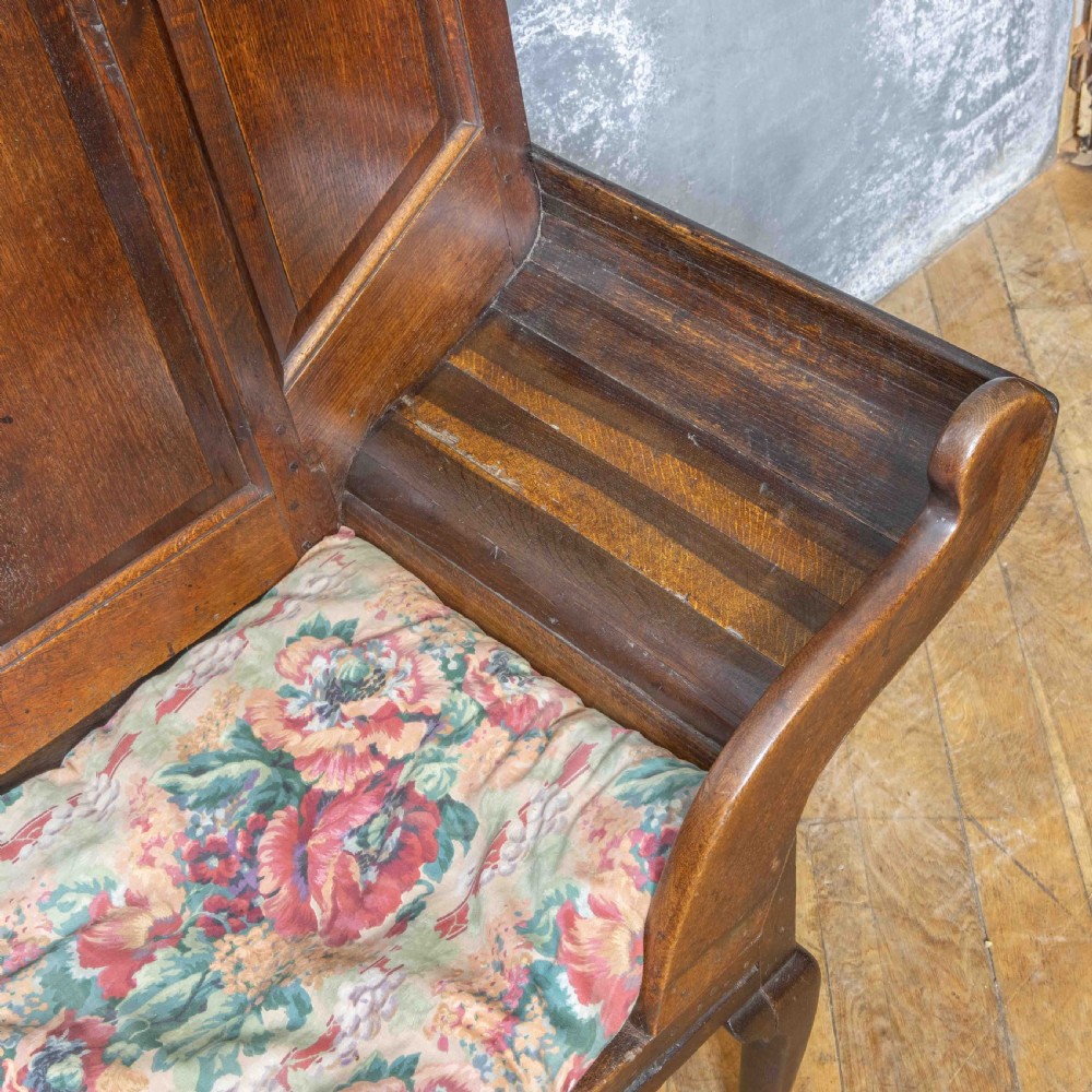 An antique dark oak sleeper settle featuring a high panelled backrest, cabriole front legs, and a floral upholstered cushion. View III