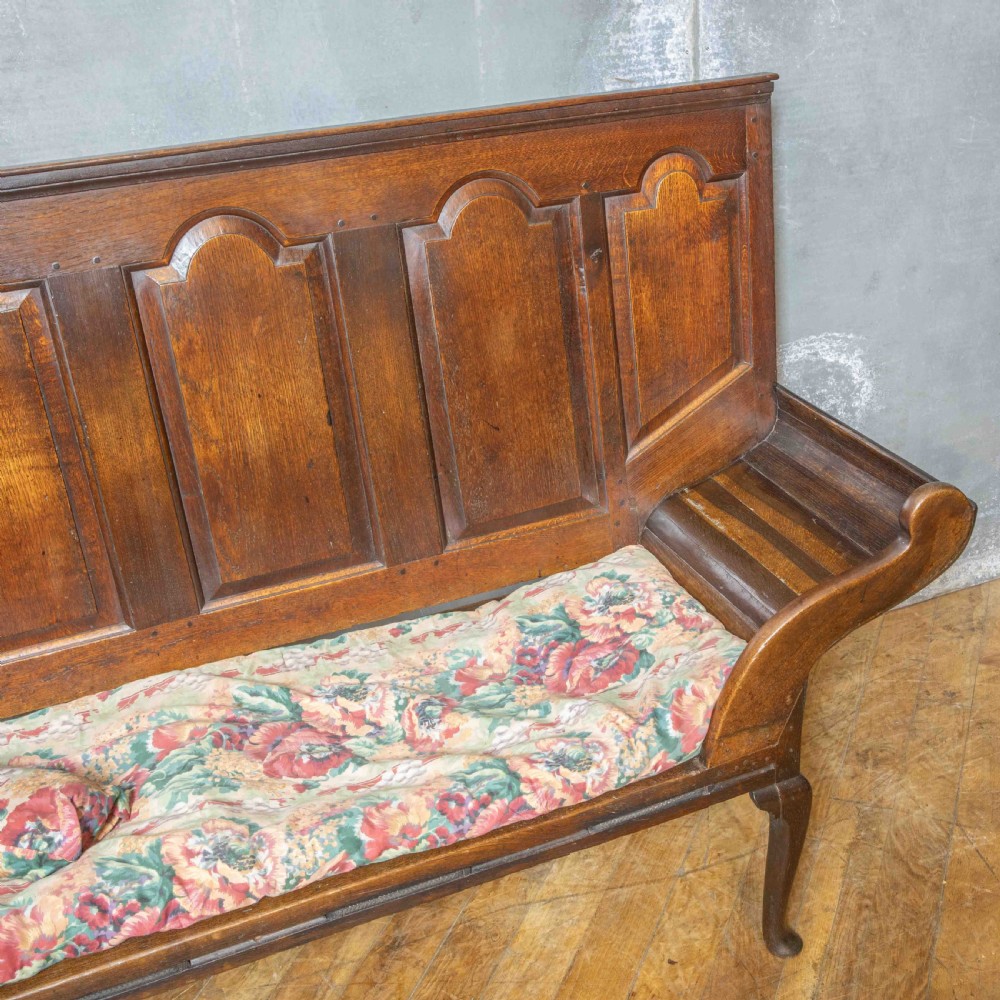 An antique dark oak sleeper settle featuring a high panelled backrest, cabriole front legs, and a floral upholstered cushion. View IV