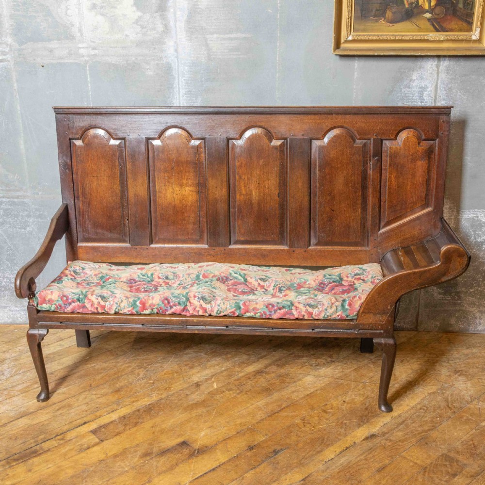 An antique dark oak sleeper settle featuring a high panelled backrest, cabriole front legs, and a floral upholstered cushion. View V