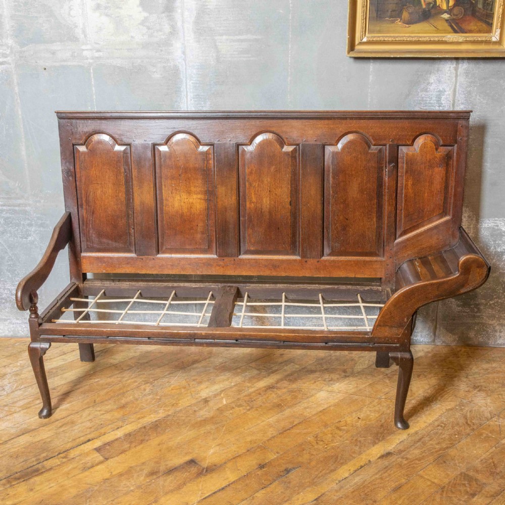 An antique dark oak sleeper settle featuring a high panelled backrest, cabriole front legs, and a floral upholstered cushion. View VI