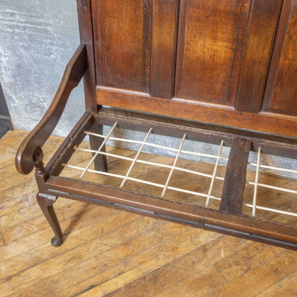 An antique dark oak sleeper settle featuring a high panelled backrest, cabriole front legs, and a floral upholstered cushion. View VII